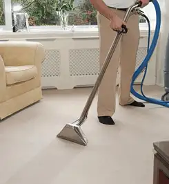 Professional carpet cleaner using a hot-water extraction wand and hose machine in a living room in Syracuse, NY.