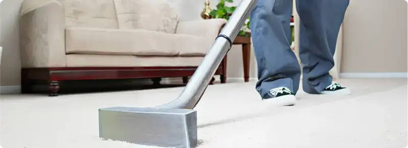 Carpet cleaning technician using a hot-water extraction wand on a light-colored carpet in a living room, Syracuse, NY.