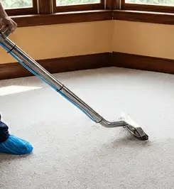 Steam carpet cleaning technician using a hot-water extraction wand on a residential carpet, wearing blue protective shoe covers Syracuse, NY.