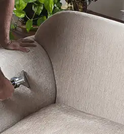 Professional upholstery cleaner deep-cleaning a fabric sofa with a handheld extraction tool and hose Syracuse, NY.