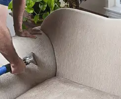 Professional upholstery cleaner deep-cleaning a fabric sofa with a handheld extraction tool and hose in Syracuse, NY.